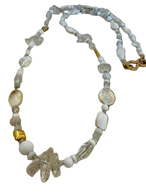 Beaded necklace with white, clear, and gold beads on a textured beige fabric background